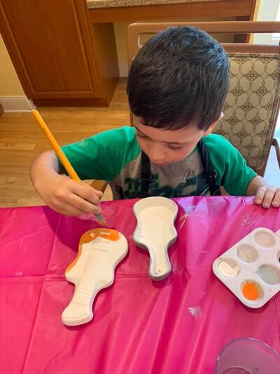 Boy carefully painting a ceramic piece at a craft table