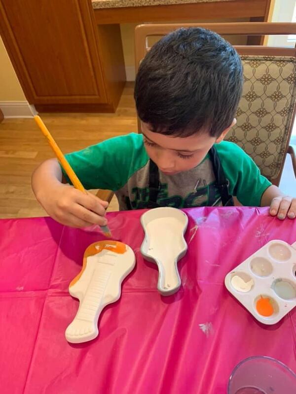 Boy carefully painting a ceramic piece at a craft table