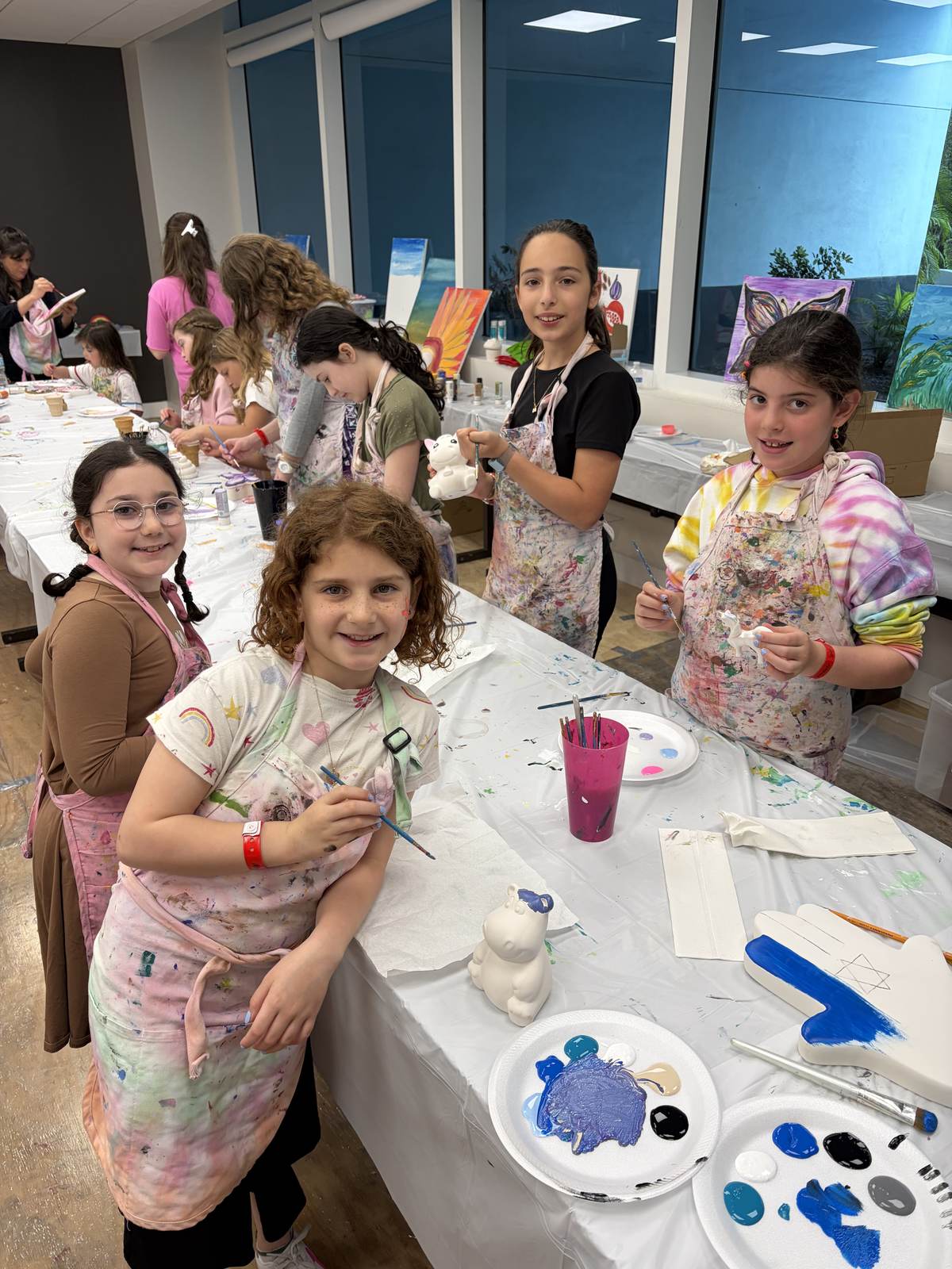 Girls in aprons painting ceramics at a long party table