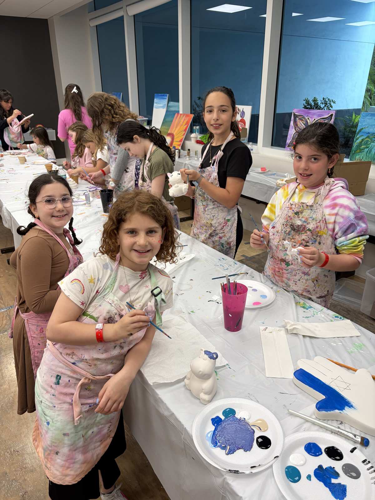 Girls in aprons painting ceramics at a long party table