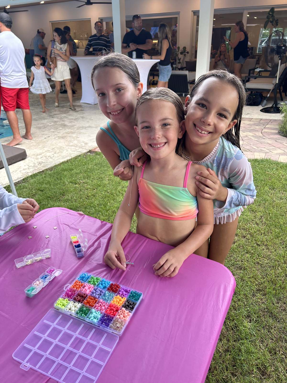 Three girls making beaded bracelets at an outdoor party table
