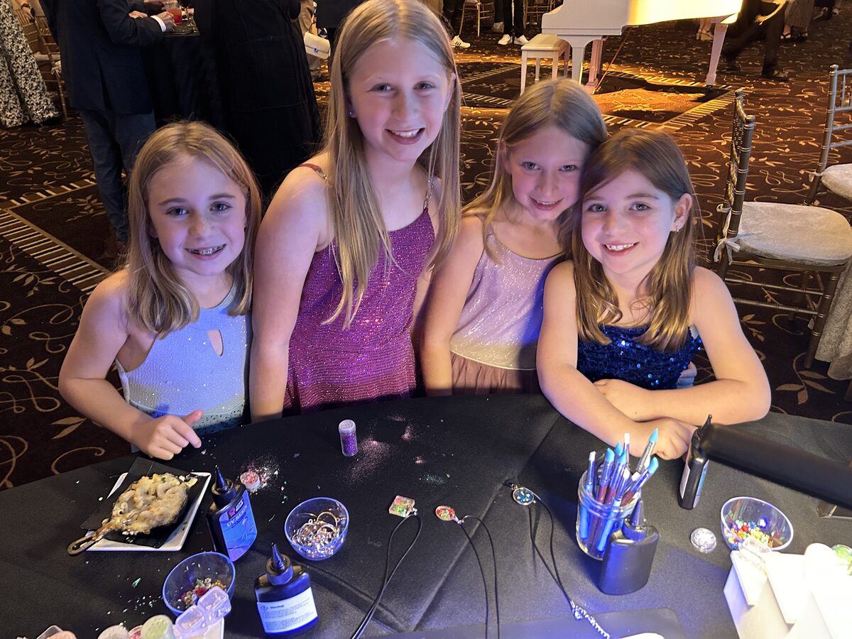 Four girls in party dresses making resin jewelry at a ballroom station