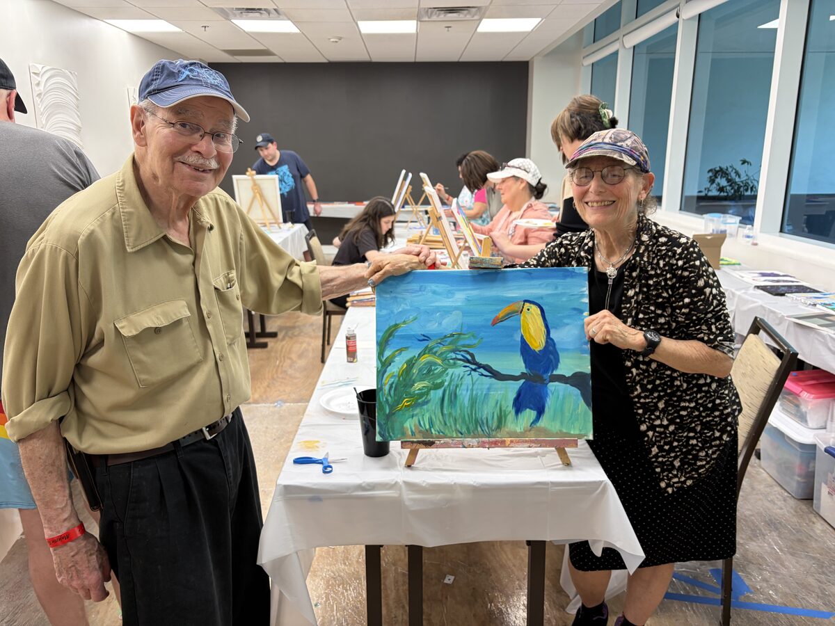 Couple holding a finished toucan canvas painting at a painting event