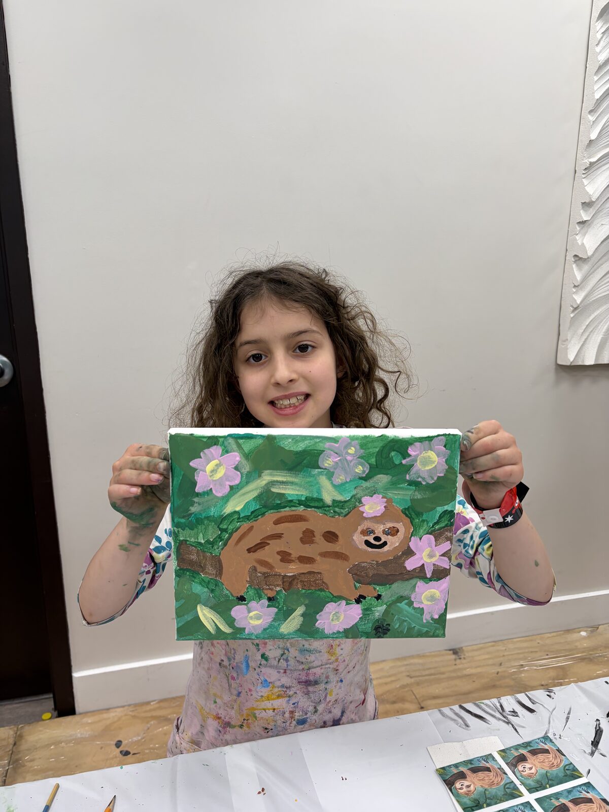 Girl holding up a finished sloth canvas painting