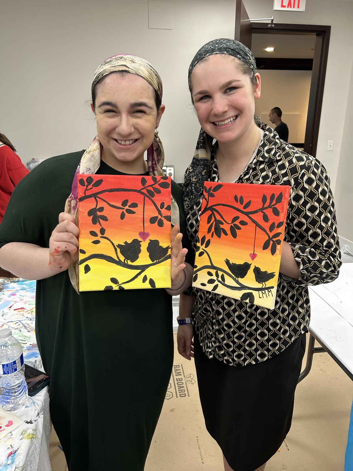 Two guests holding matching sunset canvas paintings they painted