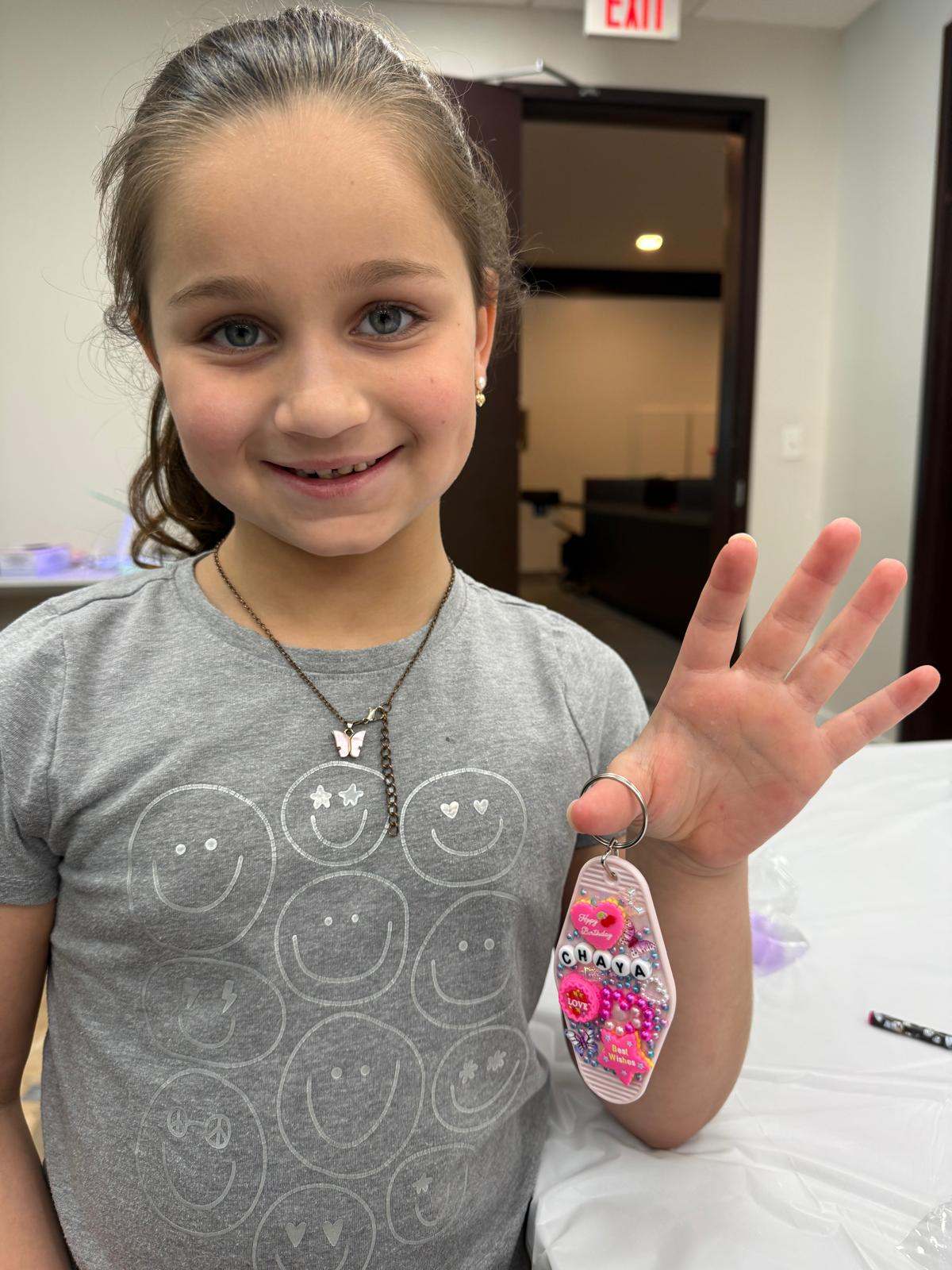 Girl smiling and holding up a resin keychain she made