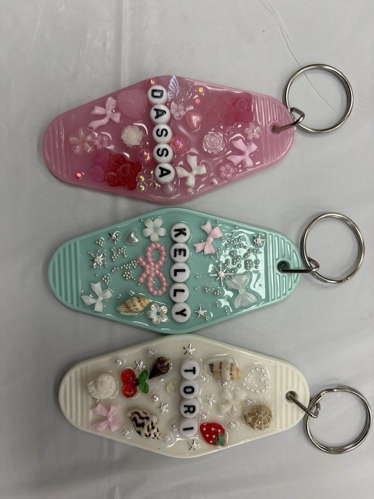 Three personalized resin keychains with names and embedded charms