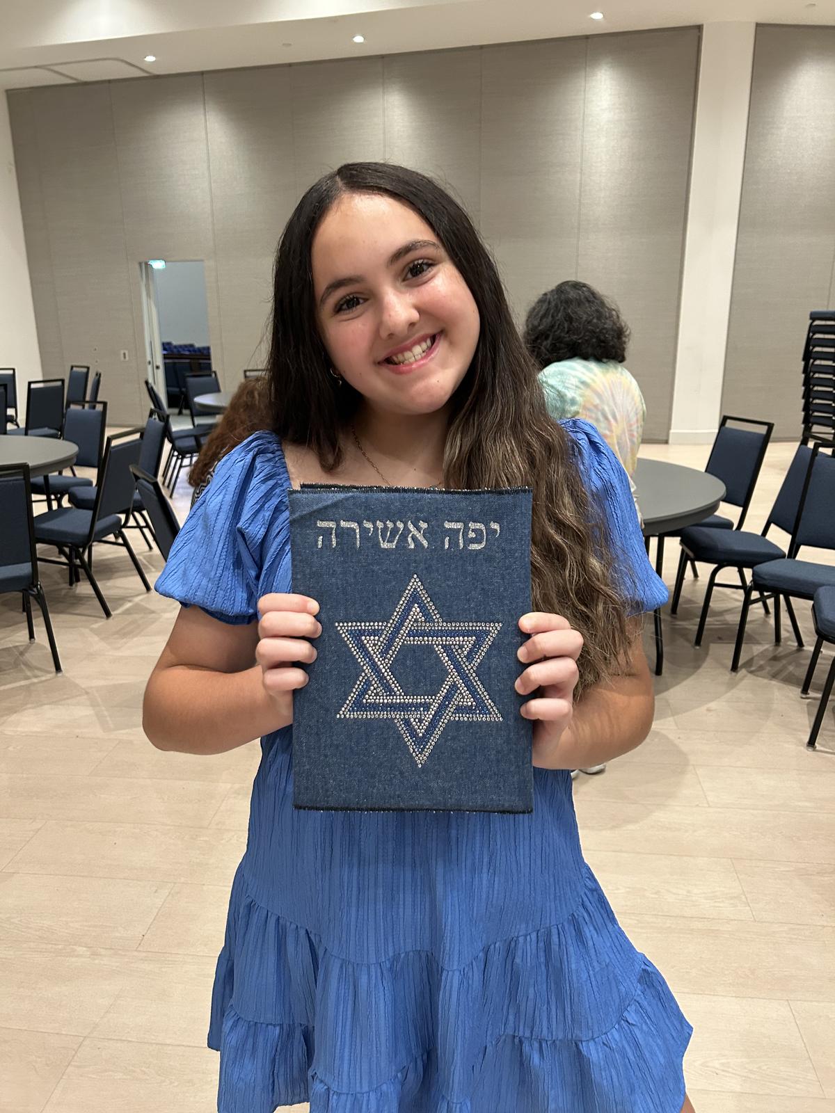 Girl holding a denim siddur cover decorated with a rhinestone Star of David and her Hebrew name