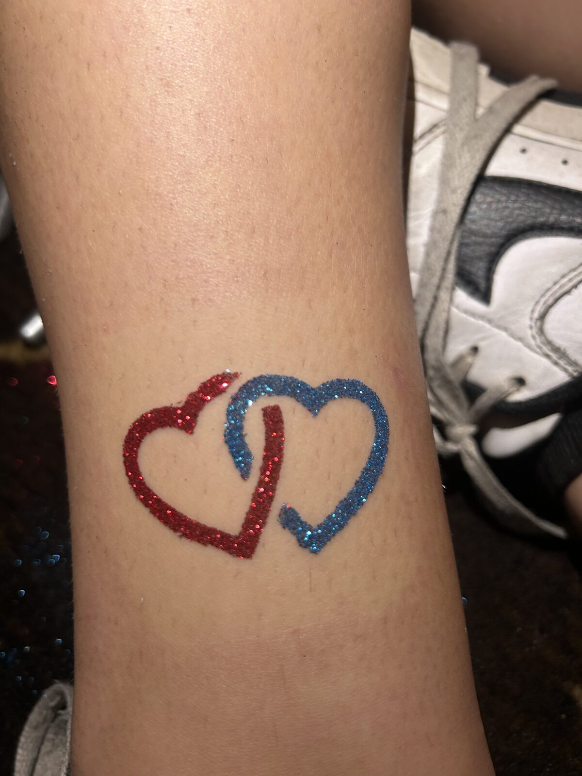 Interlocking red and blue heart glitter tattoo on a guest's leg