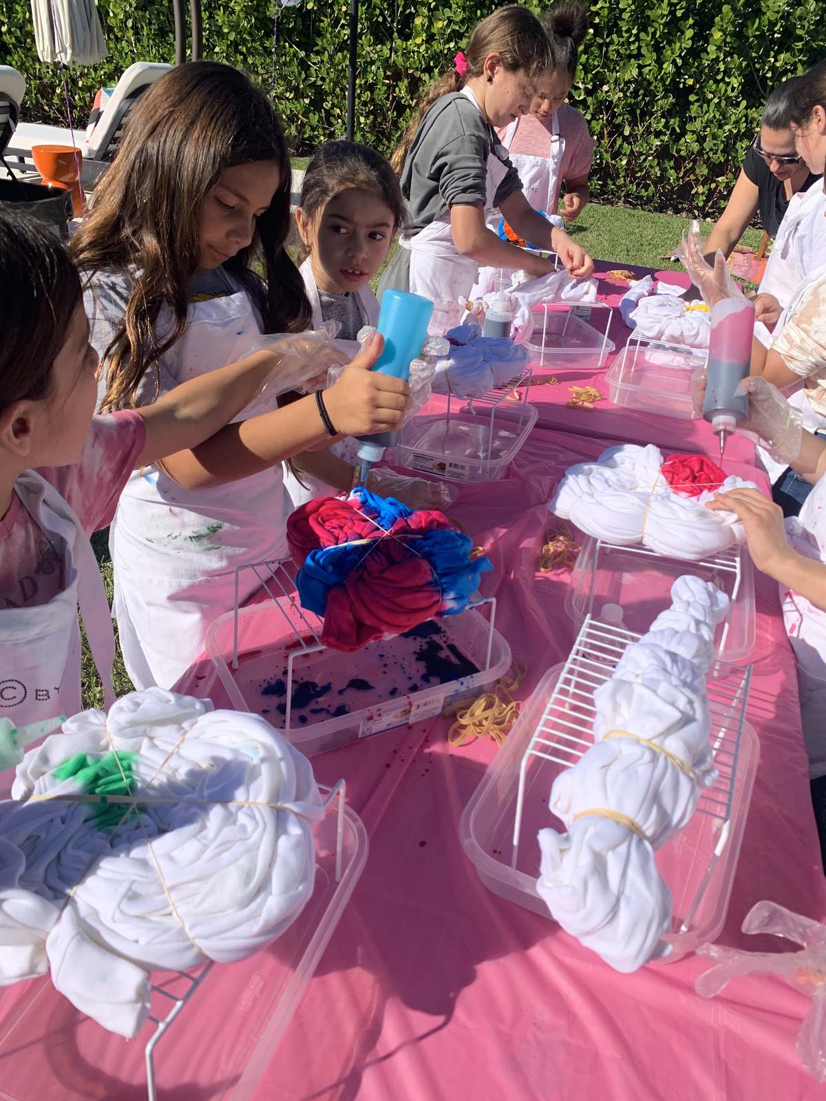 Kids tie dyeing shirts at a pink table at an outdoor party