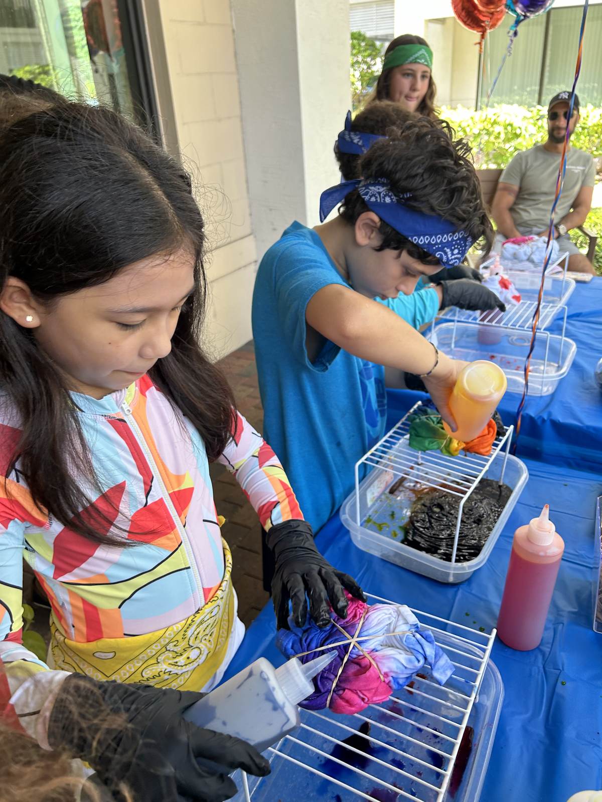 Kids tie dyeing shirts with staff help at an outdoor party