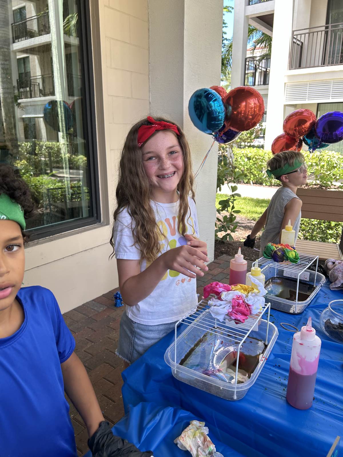 Kids at a tie dye station at an outdoor birthday party with balloons